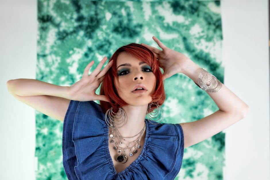 Stylish young woman posing with bold accessories against a green backdrop.