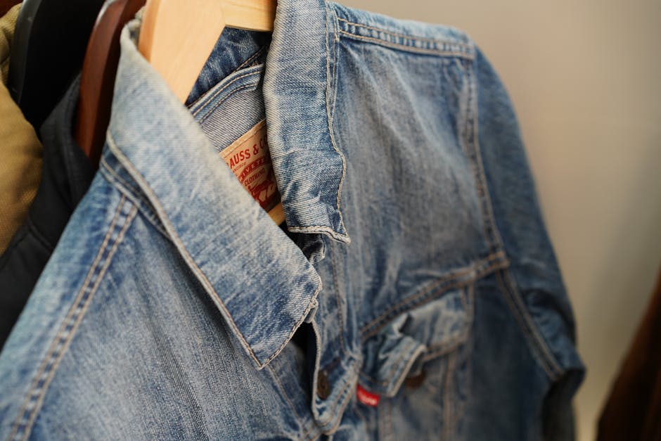 Close-up of a blue denim jacket hanging on a wooden hanger indoors.
