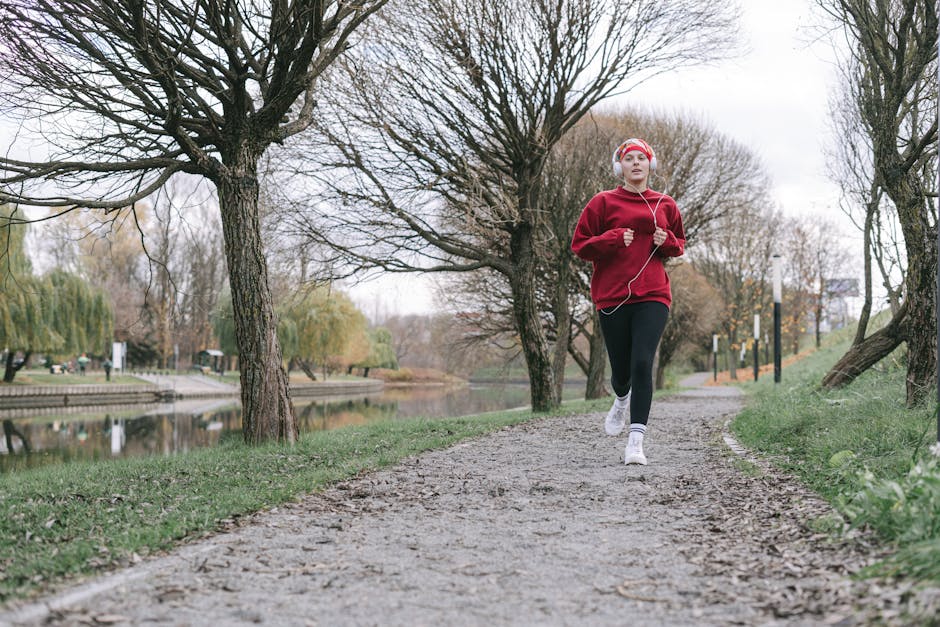 A woman in a red outfit jogs along a tree-lined path by a calm river, capturing an autumn fitness vibe.