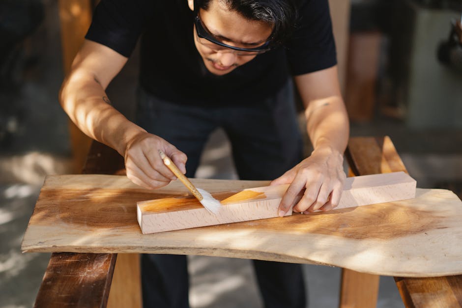 Young ethnic carpenter applying protective varnish on wooden detail while working in professional workshop