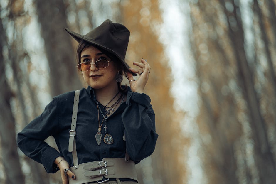 A woman posing confidently in a forest with a stylish hat and sunglasses during autumn.