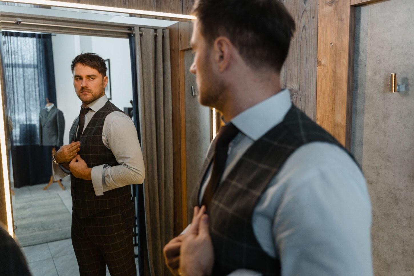 Man adjusting a vest and shirt in front of a mirror