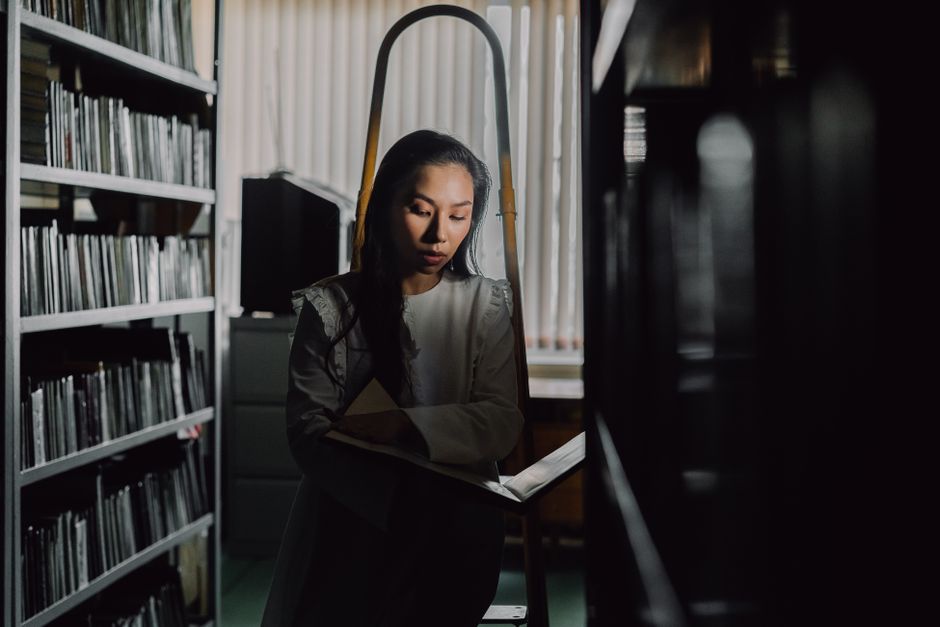A woman deeply absorbed in a book within the dim light of a quiet library.
