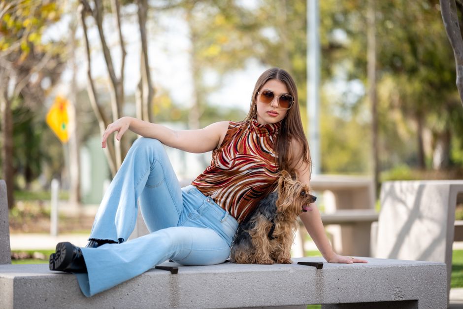 Stylish woman with sunglasses lounging on a bench with her dog in a sunny urban park.