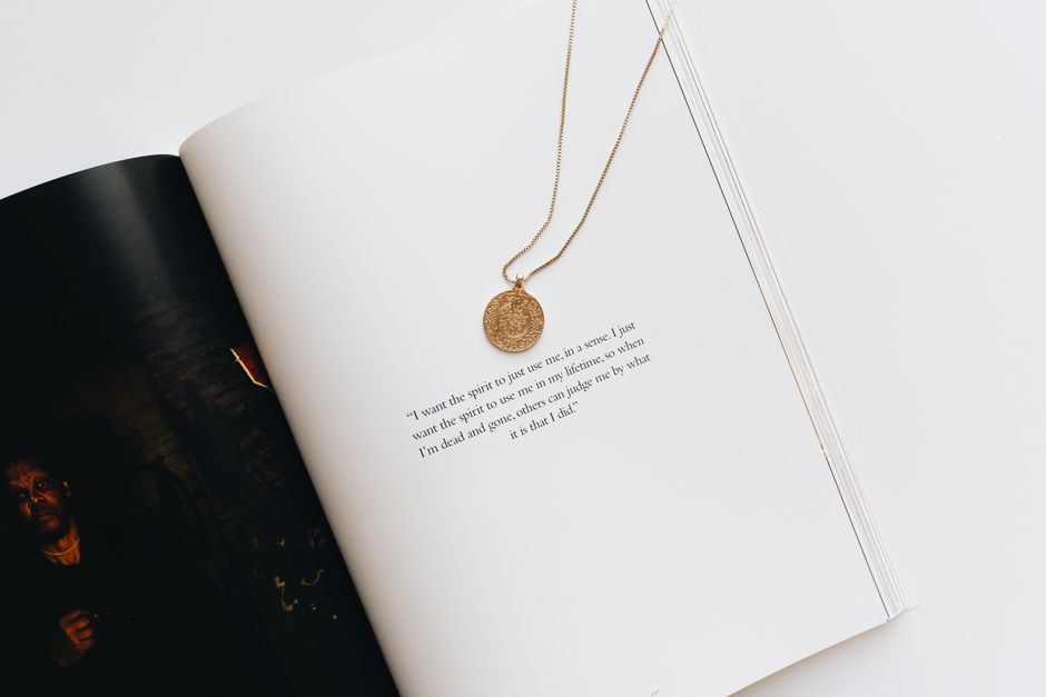 A gold necklace elegantly placed on an open book with visible text, creating a minimalist visual.