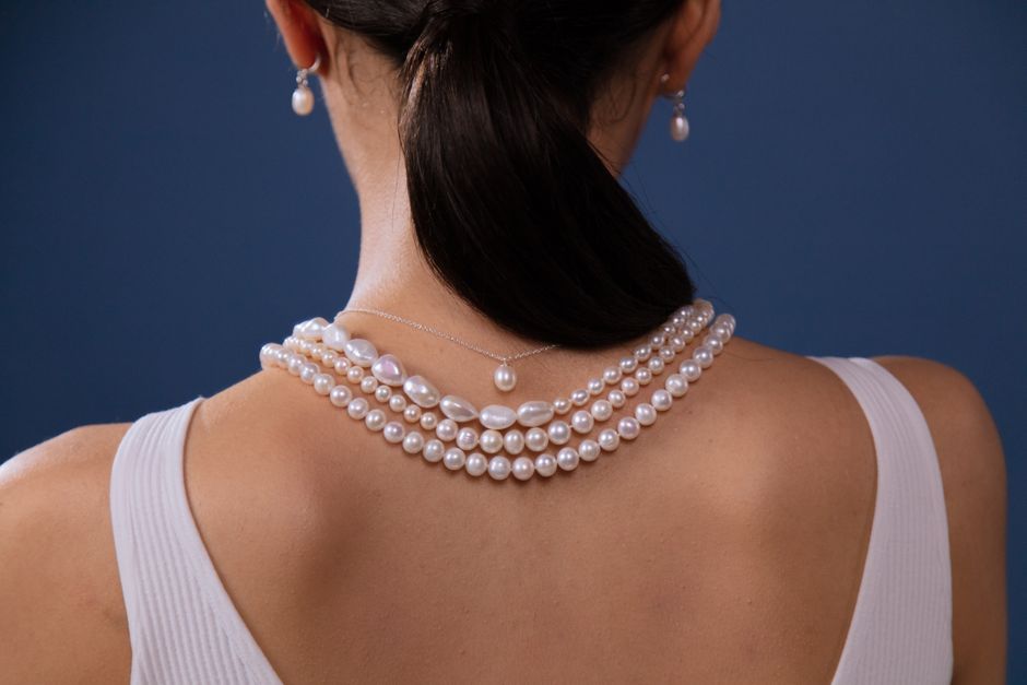 Elegant pearl necklace adorned on a woman's neck against a blue backdrop.