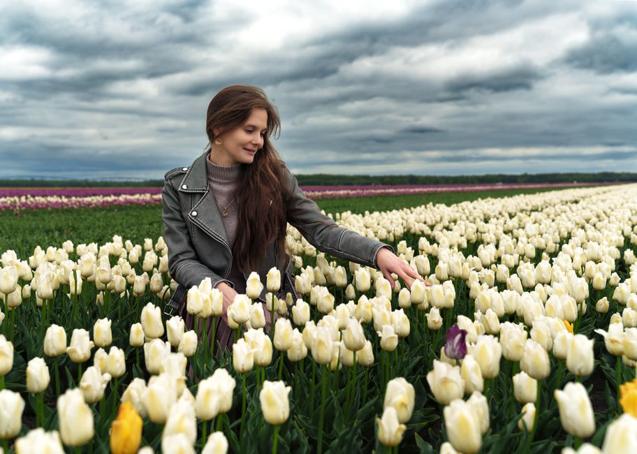 A woman enjoys a vast field of white tulips in Тышковичи, Belarus under a cloudy sky.