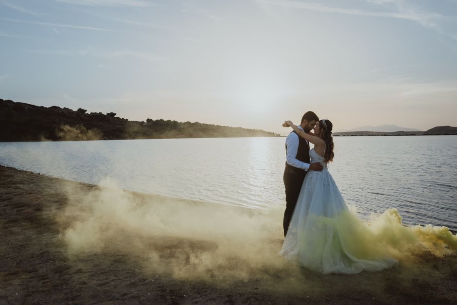 A romantic embrace of a newlywed couple on a beach at sunset with yellow smoke flares.