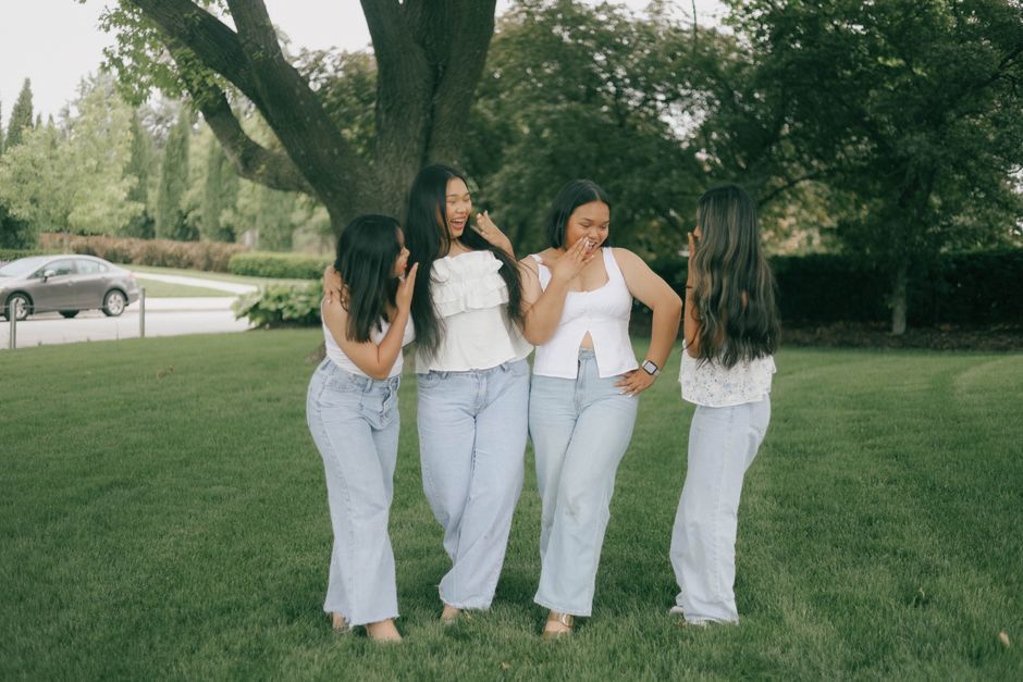 Four friends in casual attire sharing a lighthearted moment in a park under a tree.
