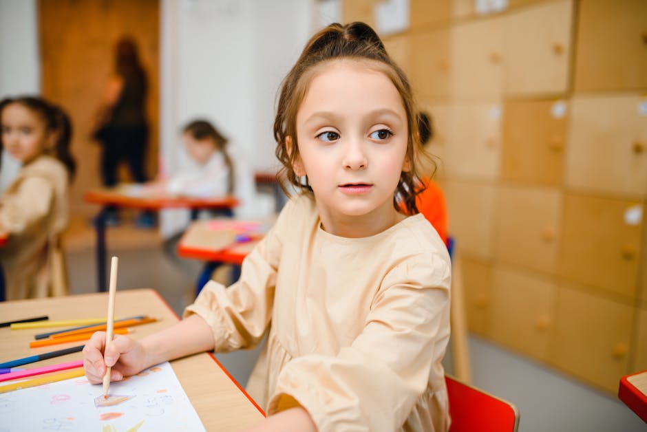 A young girl sitting at a desk coloring with crayons in an elementary school classroom.