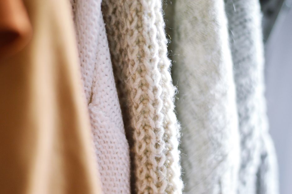 Detailed view of multiple woolen knitted sweaters in soft, neutral colors emphasizing texture and warmth.