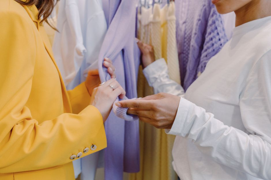 Two women examining vibrant clothing on a rack inside a boutique.