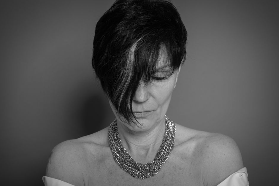 Monochrome portrait of a woman with short hair and chain necklace, eyes closed.