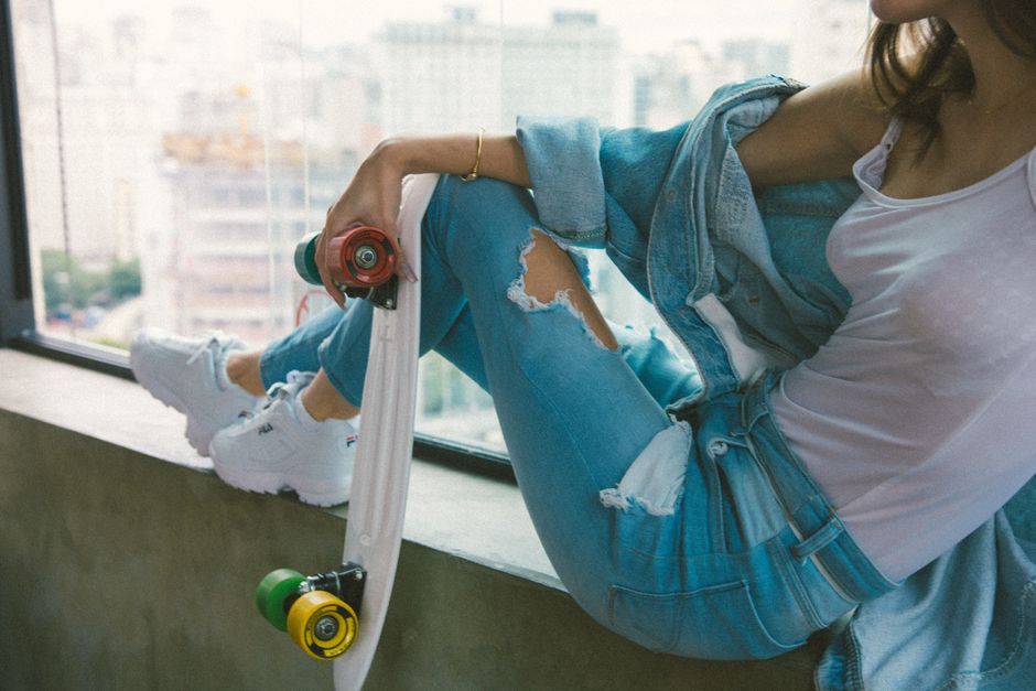 Casual urban style featuring ripped jeans, sneakers, and skateboard in a modern interior.