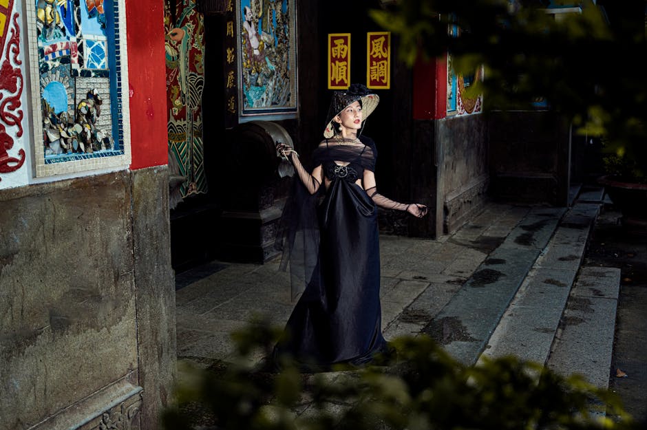 A woman in a stylish black dress poses in front of a traditional Asian temple, capturing elegance and cultural charm.