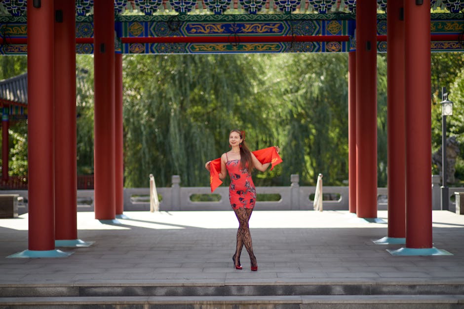 Smiling woman in red dress poses at vibrant traditional Asian gazebo.